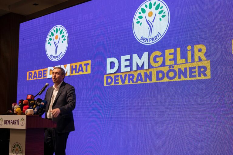 Leader of pro-Kurdish DEM party standing on stage, speaking at lectern.