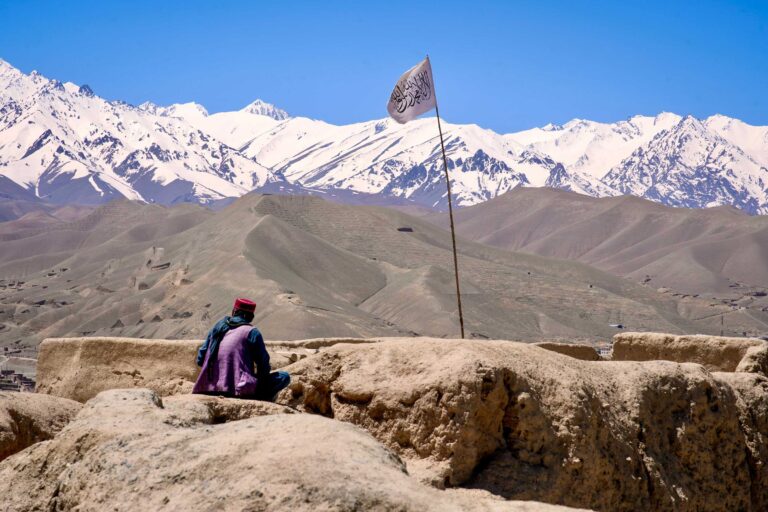 A man sits on top of Gholghola, an ancient city destroyed by Genghis Khan in the 13th century and an UNESCO World Heritage site, alongside the flag of the Islamic Emirate. Bamiyan, central Afghanistan