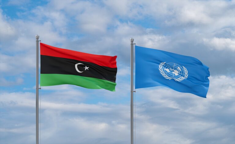 United Nations and Libya flags waving together in the wind on blue cloudy sky.
