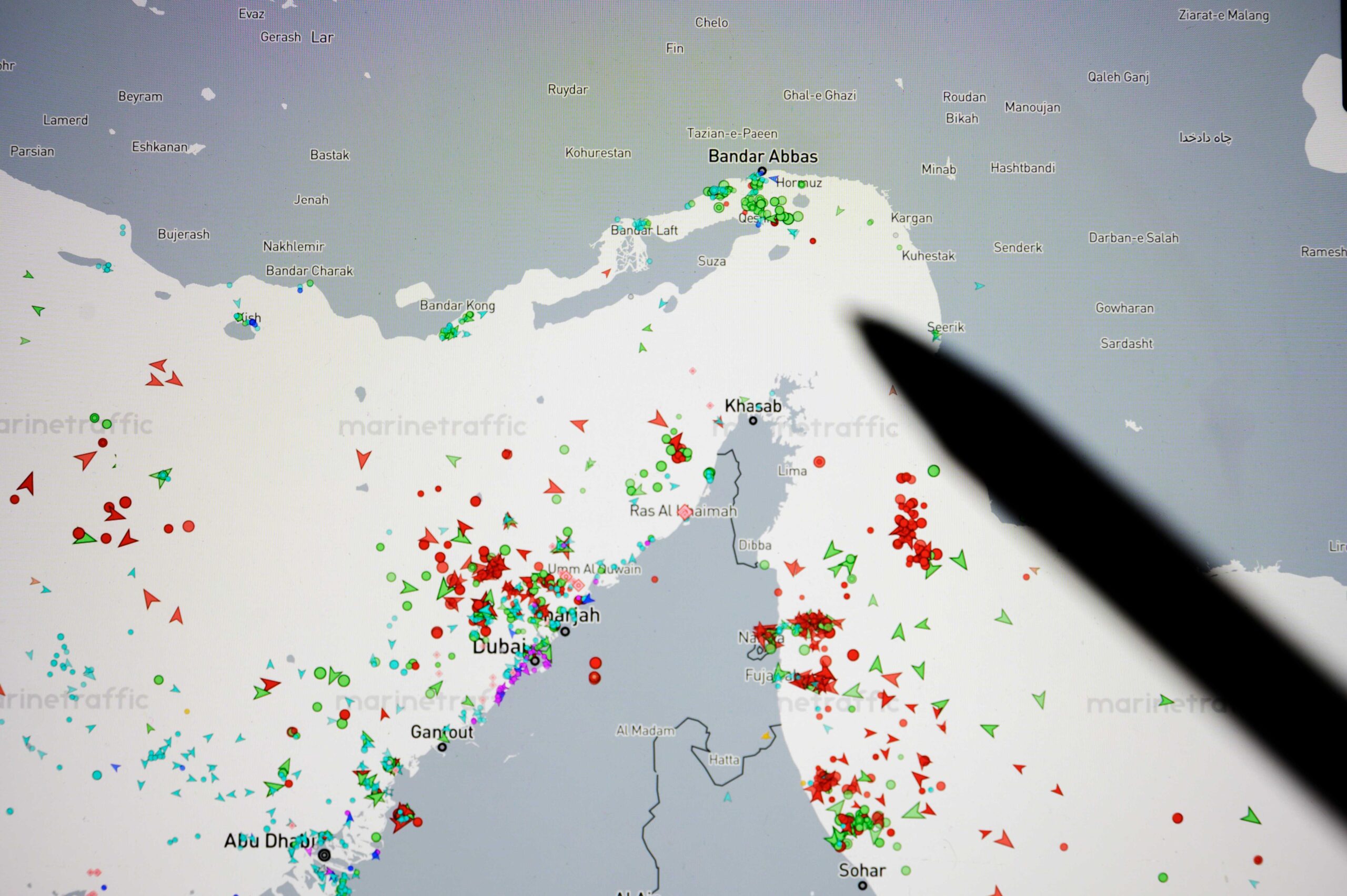 Paris, France - March 16 2026: A person points with a pen to the Strait of Hormuz on a digital map showing live maritime vessel tracking via the MarineTraffic website.