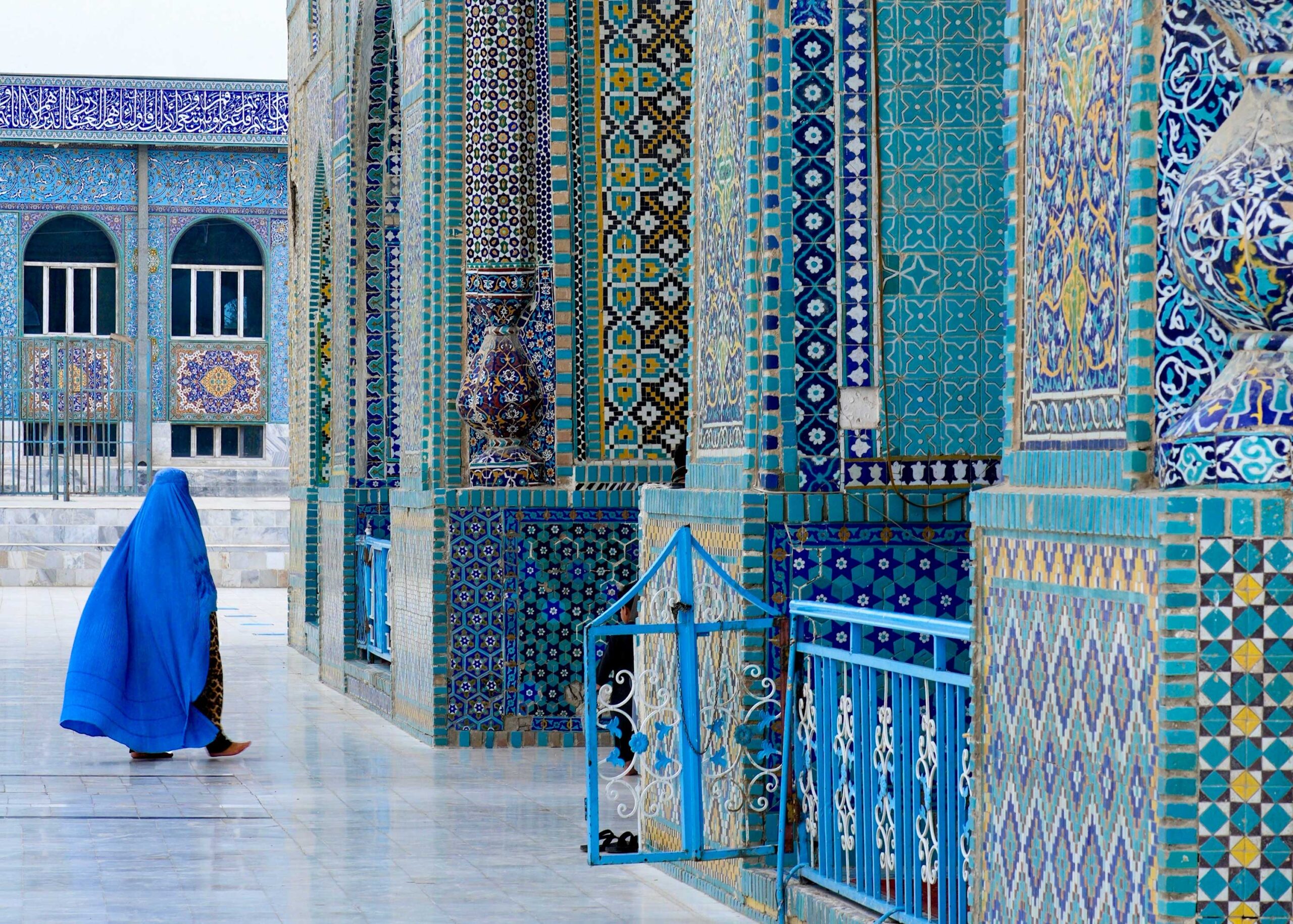Mazar-i-Sharif, Afghanistan - 05 09 2024: A woman in a blue Afghan burka walks towards the entrance of Hazrat Ali Shrine, also known as The Blue Mosque.