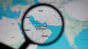 Close up of map showing Strait of Hormuz and Persian Gulf region under magnifying glass, highlighting geopolitical tensions, oil supply routes, and strategic location between Iran, Oman and UAE waters