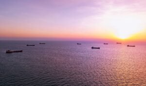 Cargo ships anchored at sunset in open ocean waters near Hormuz.