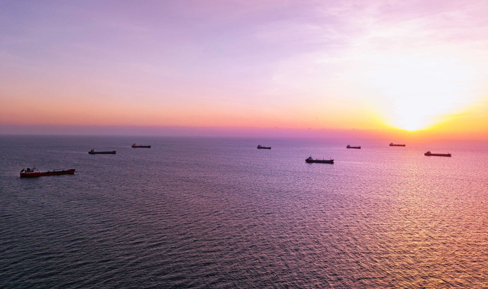 Cargo ships anchored at sunset in open ocean waters near Hormuz.