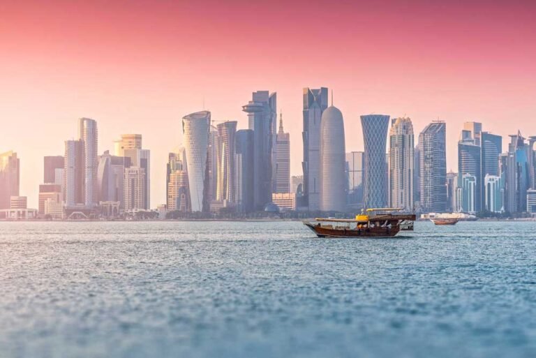 Doha city skyline featuring West Bay skyscrapers along the Persian Gulf during a beautiful pastel sunset, with dhow boats sailing